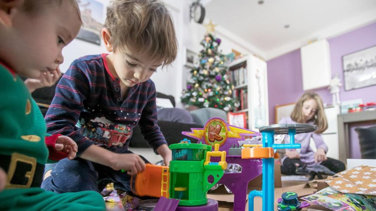 Dos niños juegan con uno de los regalo mientras una niña desenvuelve otro.-SANTI OTERO