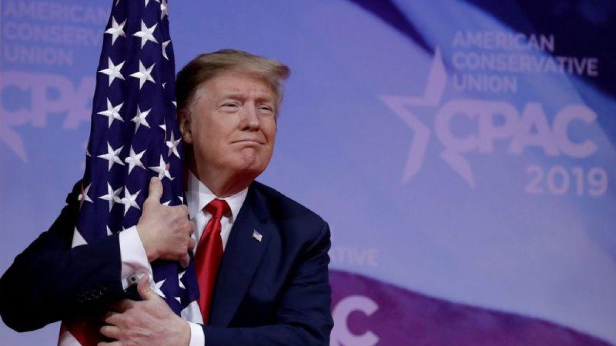 El presidente Donald Trump abrazando una bandera de su país.-REUTERS