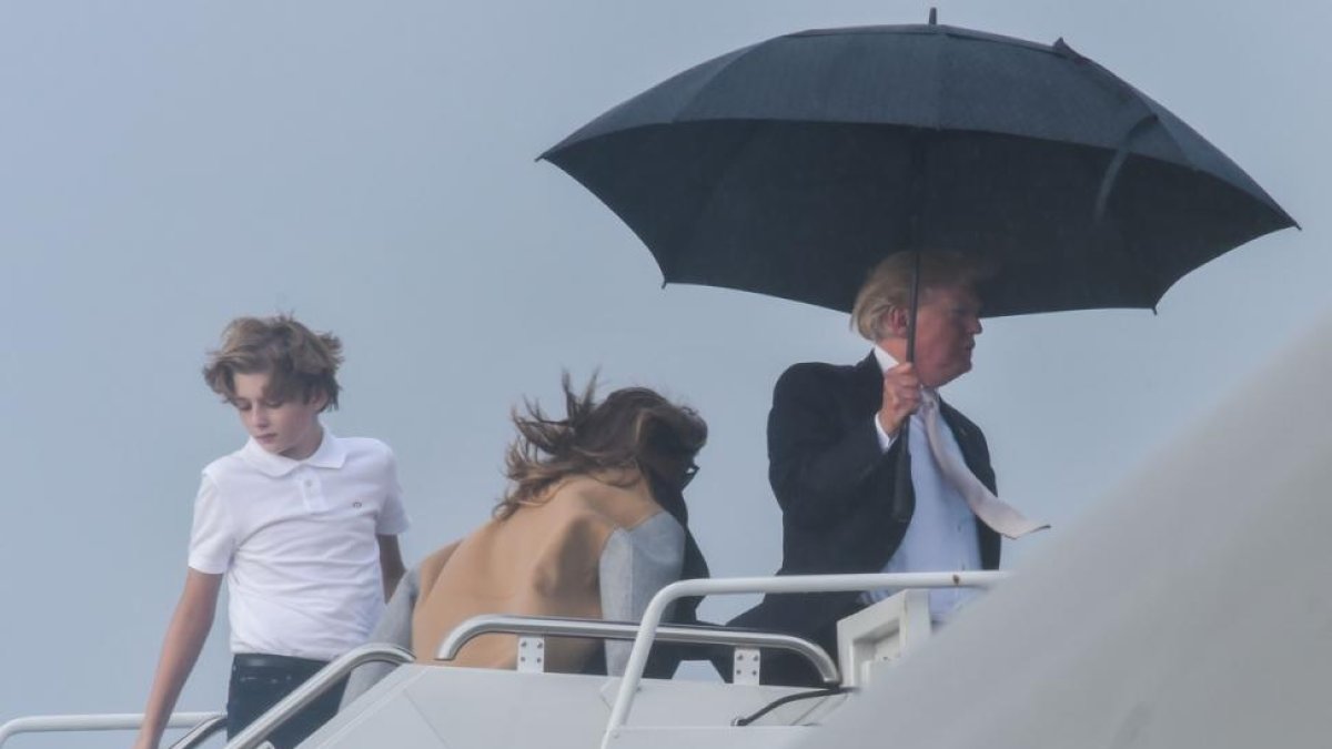 El presidente de EEUU, Donald Trump, sostiene un amplio paraguas para protegerse de la lluvia, mientras espera a su mujer Melania y a su hijo Barron, durante el embarque del Air Force One en Flordia.-/ AFP / NICHOLAS KAMM (AFP)