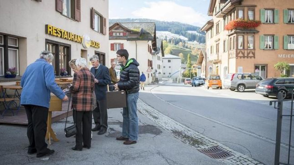 Residentes en la población suiza de Obersaxen Meierhof depositan su voto en urnas colocadas en el exterior de un colegio electoral, este domingo.-EFE / GIAN EHRENZELLER