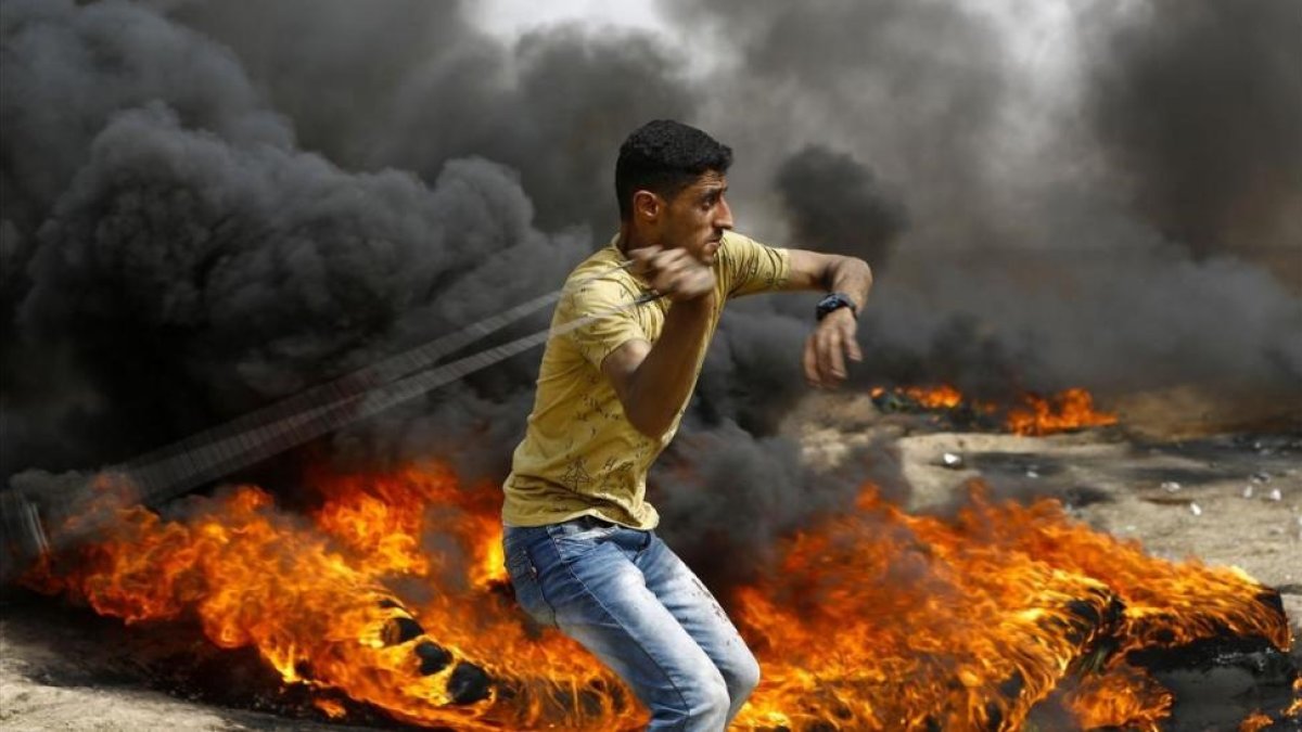 Un palestino se dispone a lanzar piedras entre los neumáticos incendiados contra las tropas israelís, en las protestas junto a la frontera de la Franja de Gaza, el 20 de abril.-/ AFP / MOHAMMED ABED