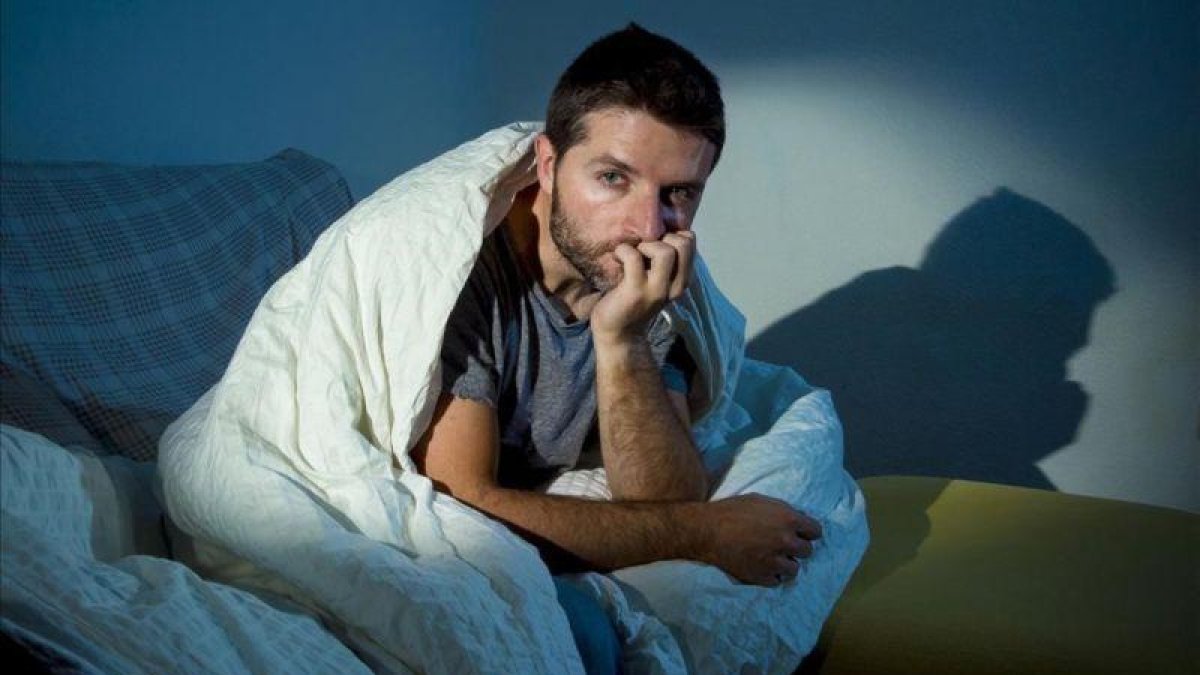 Hombre sentado en el sofá por la noche con miedo.-123RF