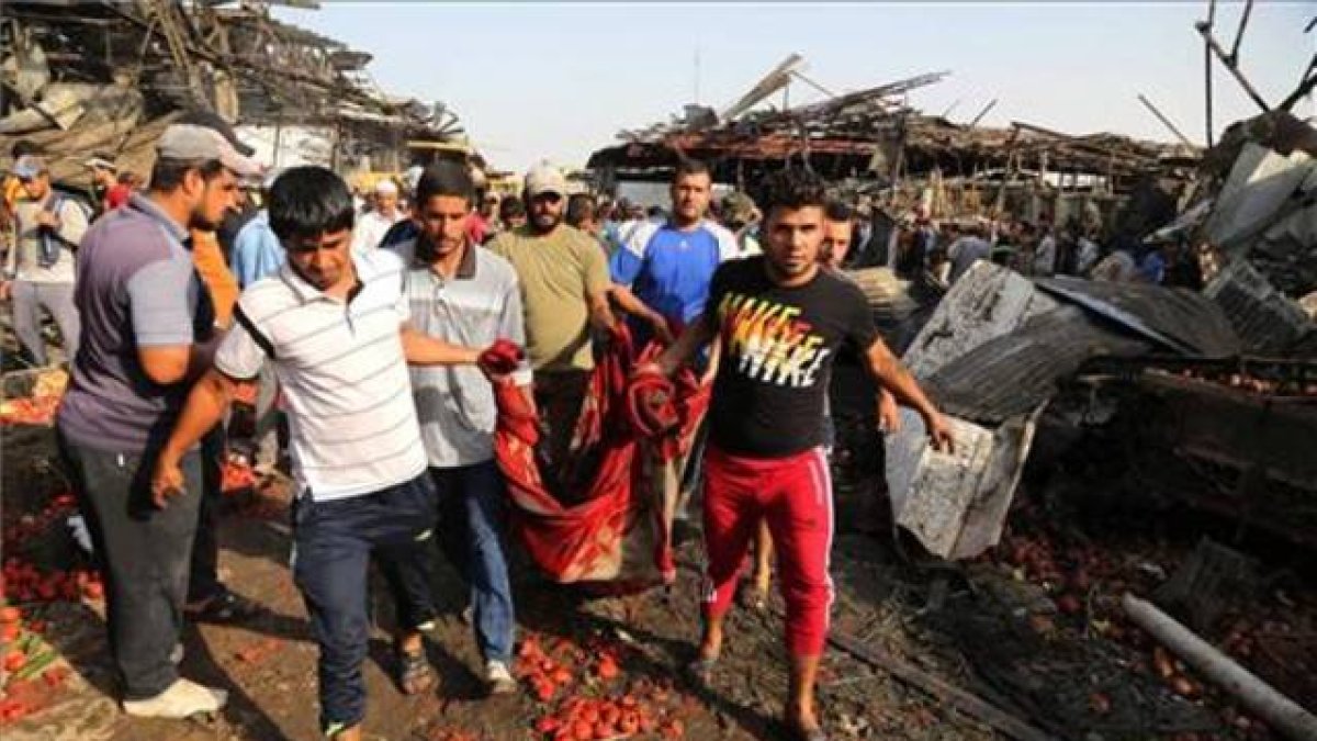 Un grupo de hombres evacúa el cuerpo sin vida de una víctima del atentado perpetrado con un caimión bomba en el mercado de Yamila.-AP / KARIM KADIM