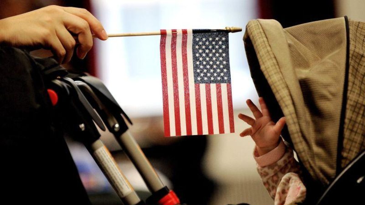Imagen muestra a un bebe que intenta alcanzar la bandera estadounidense que sostiene su madre en Nueva York.-EPA