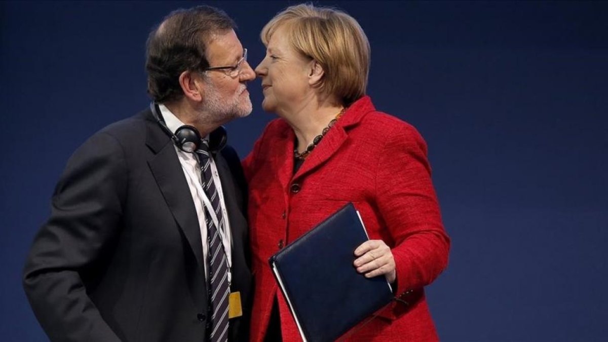 Rajoy y Merkel se saludan durante un congreso del Partido Popular Europeo.-EL PERIÓDICO