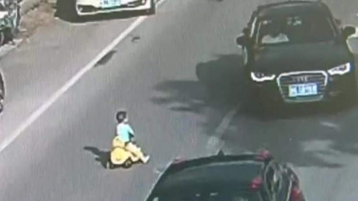 Un niño chino se mete con su coche de juguete en una autopista en hora punta.-