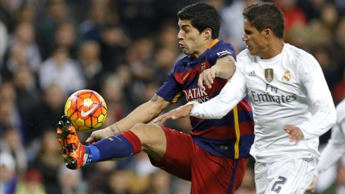 Varane y Luis Suárez luchan por un balón en el clásico del pasado año en el Bernabeú.-AP / FRANCISCO SECO