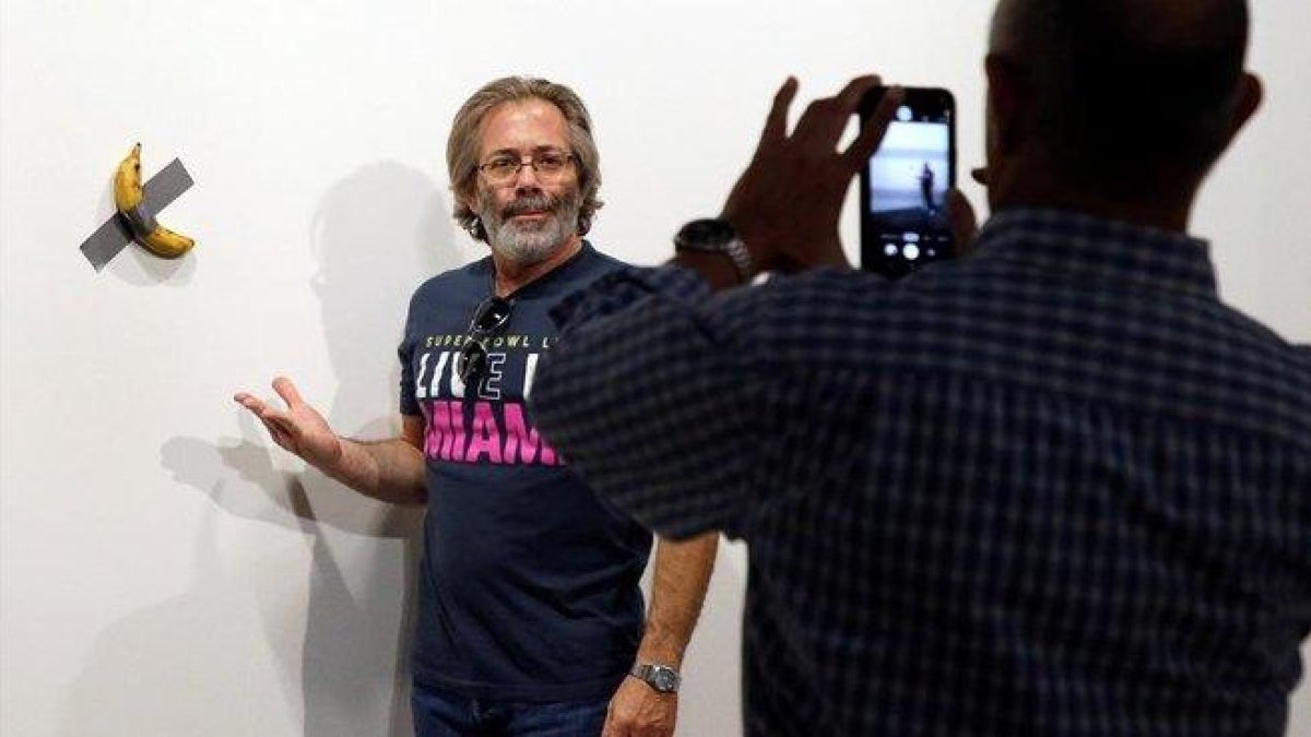 Un hombre se retrata junto a la obra del artista italiano Maurizio Cattelan.-RHONA WISE / EFE