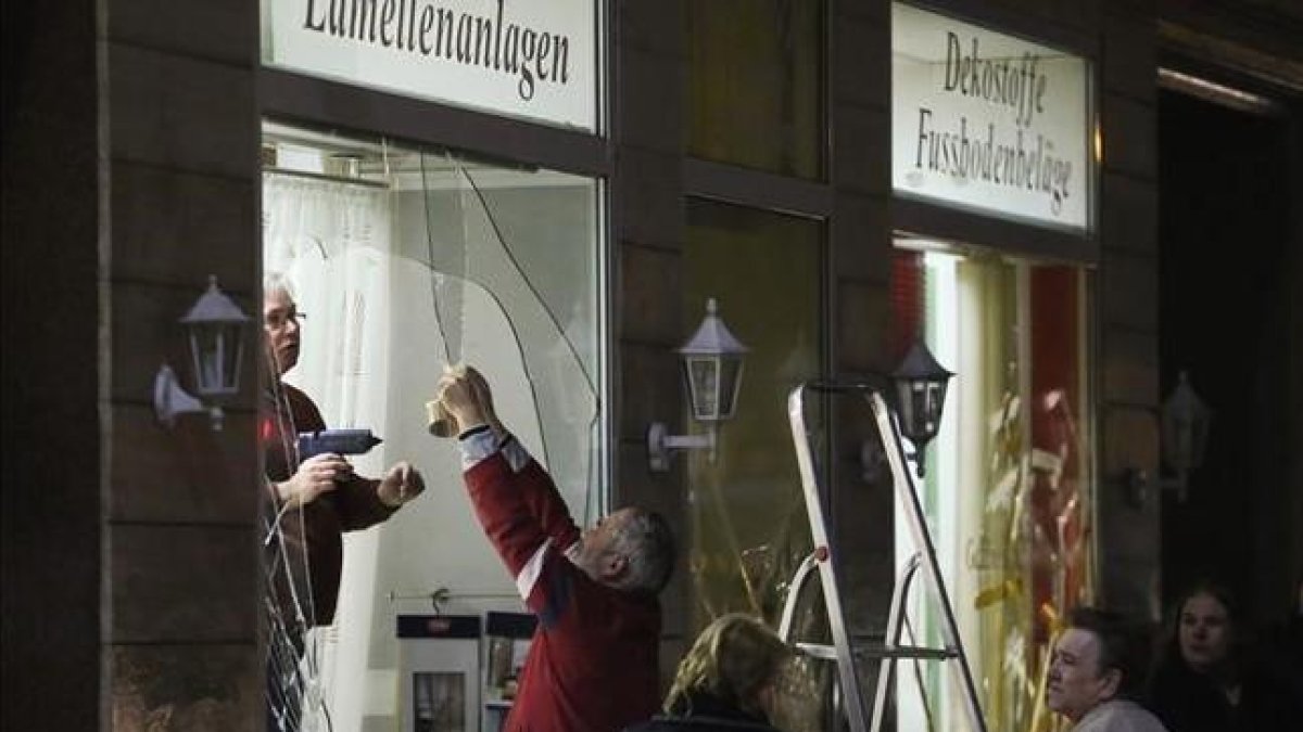 Unos hombres reparan los escaparates de una tienda rotos por los manifestantes ultraderechistas en Leipzig.-AFP / JAN WOITAS