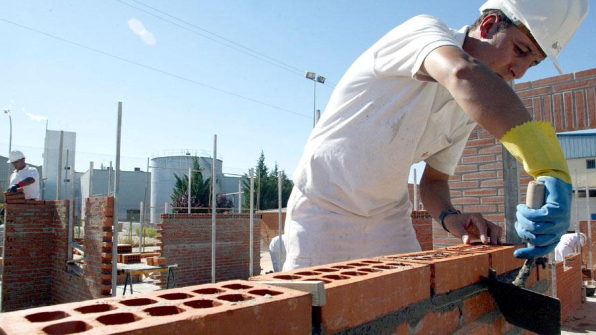 Un albañil trabaja levantando una pared en una obra junto con otros profesionales de la construcción.-ICAL