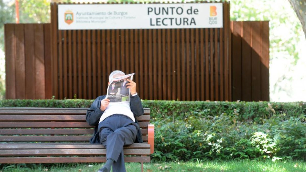 Un hombre lee el periódico junto al punto de lectura del paseo de la Isla.-ISRAEL L. MURILLO