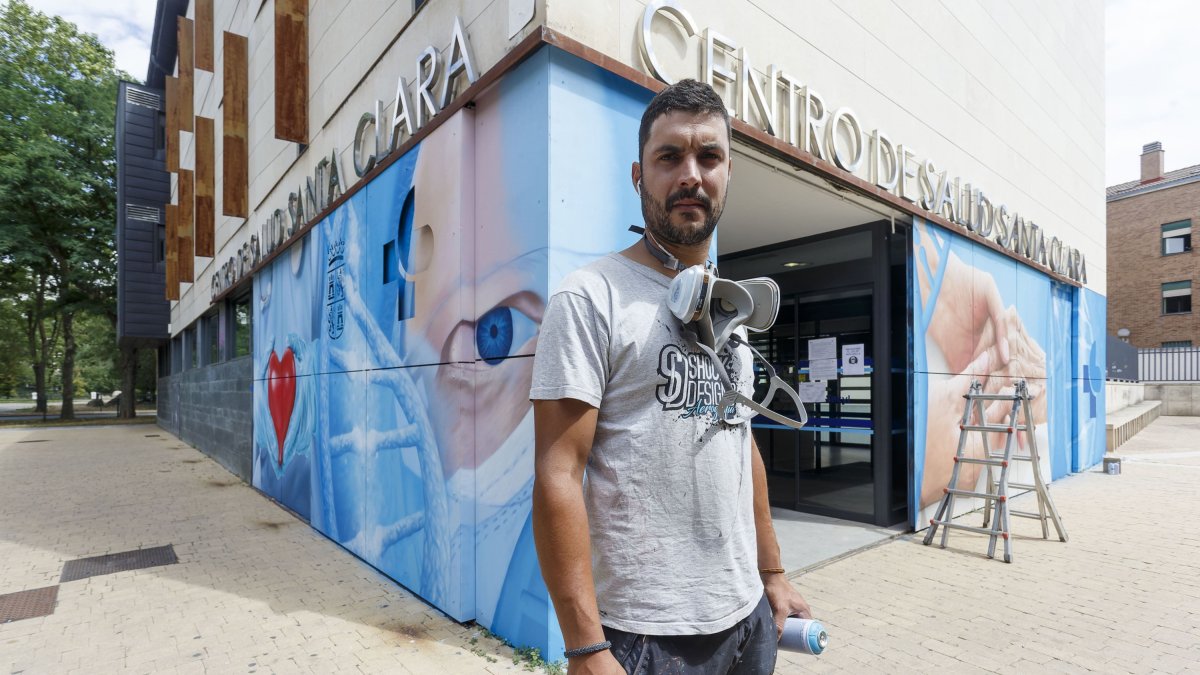 Christian Saldaña posa ante el espectacular mural que está rematando en el centro de Salud de Santa Clara. FOTOS: © ECB / SANTI OTERO