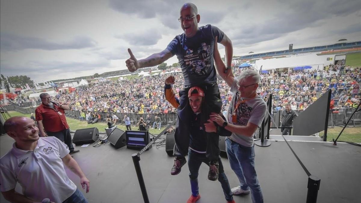 Marc Márquez levanta sobre sus hombros al aficionado que pujó, en la subasta solidaria de Silverstone, por hacerse un selfie con él. /-MOTOGP.COM / DIEGO SPERANI