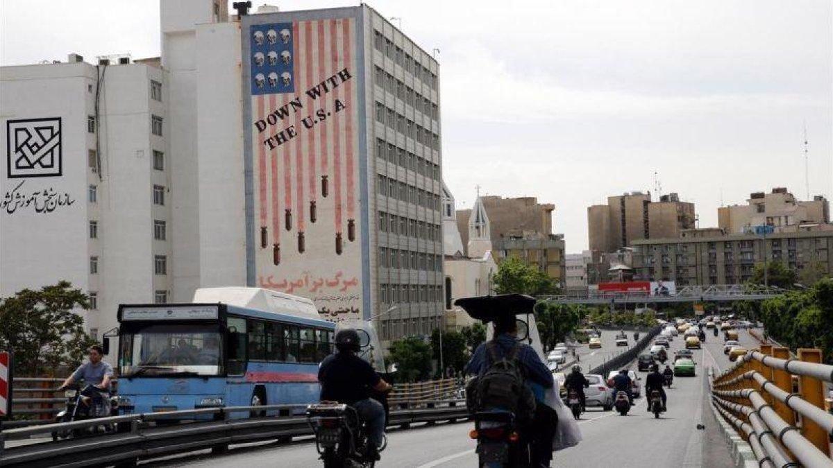 Conductores iranís circulan junto a un edificio en el que aparece una pintada contra Estados Unidos en Teherán.-EFE / ADEDIN TAHERKENAREH