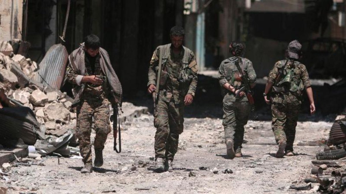 Combatientes de las Fuerzas Democráticas de Siria caminan sobre los escombros de tiendas y edificios dañados por la batalla en la ciudad de Manbij.-RODI SAID (REUTERS)