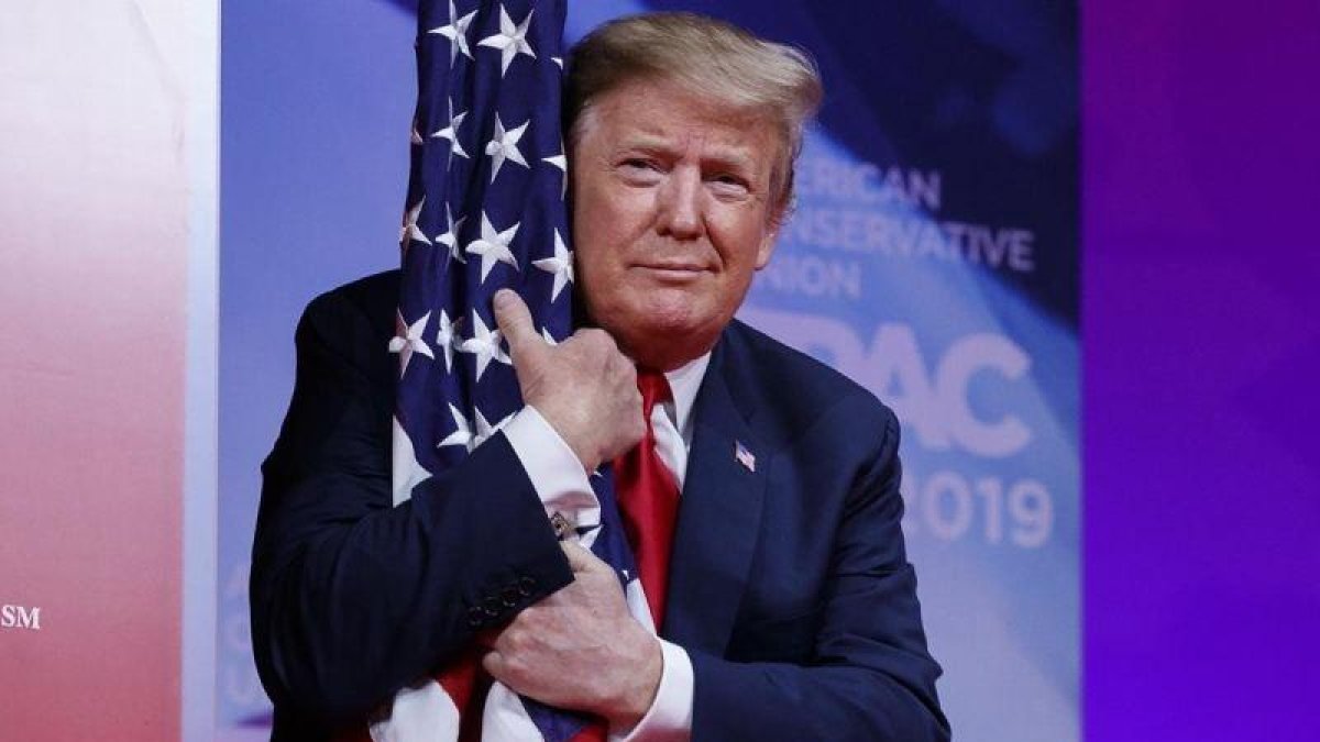 El presidente Donald Trump abraza la bandera de Estados Unidos en la Conferencia de Acción Política Conservadora.-AP / CAROLYN KASTER