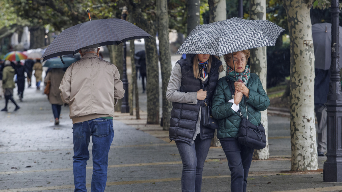 Varias personas con paraguas en el paseo del Espolón de Burgos.