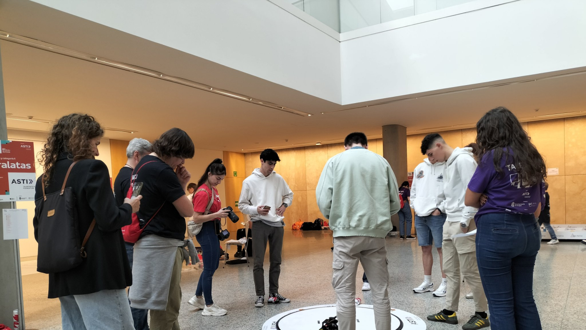 Un grupo de participantes prueban las habilidades de su robot para tirar las latas fuera del círculo.