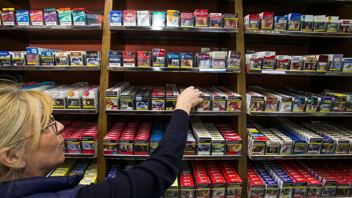 La dependienta de un estanco coge una cajetilla de tabaco del casillero de venta del establecimiento.