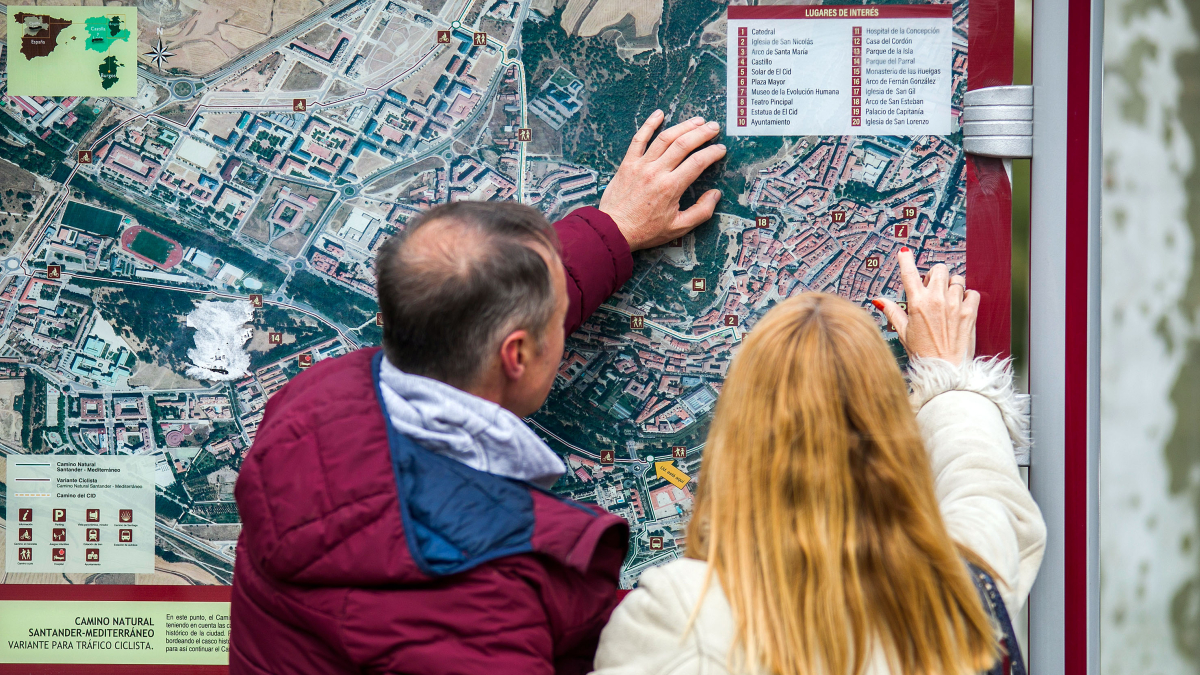 Dos turistas consultan uno de los mapas de la ciudad de Burgos instalado en un Mupi.