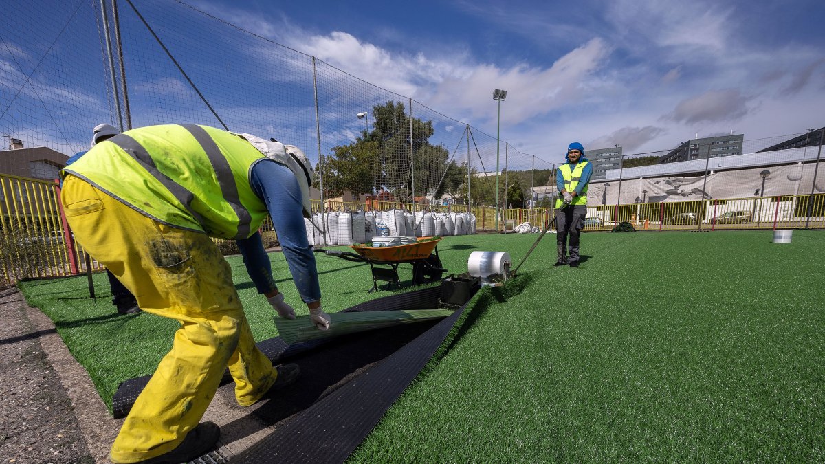 Dos operarios ajustan el nuevo césped artificial del campo de fútbol siete del complejo deportivo José Luis Talamillo.