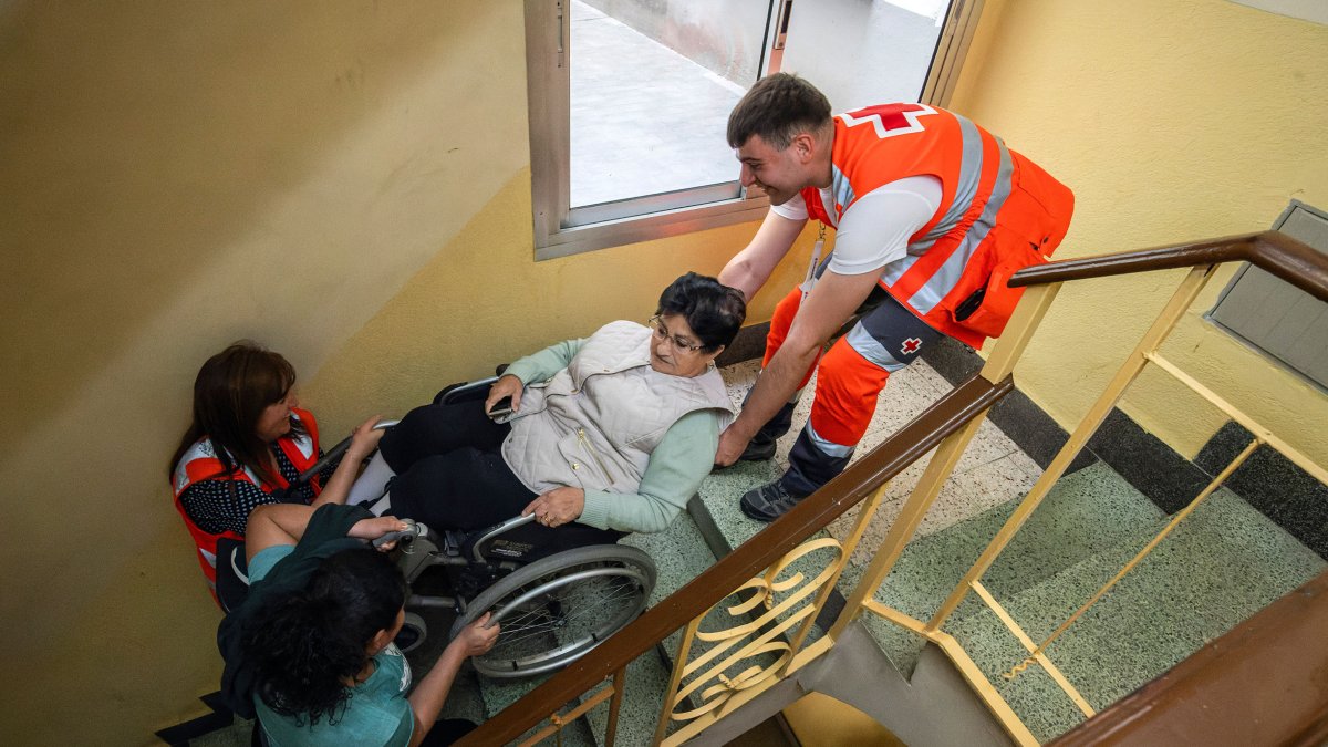 Sin luz, los ascensores dejaron de funcionar y en la imagen los voluntarios de Cruz Roja asisten a una mujer en silla de ruedas en la escalera de su edificio.