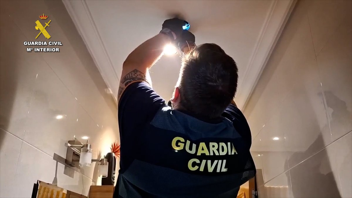 Un agente de la Guardia Civil desmonta la cámara instalada en el sistema de iluminación del baño.