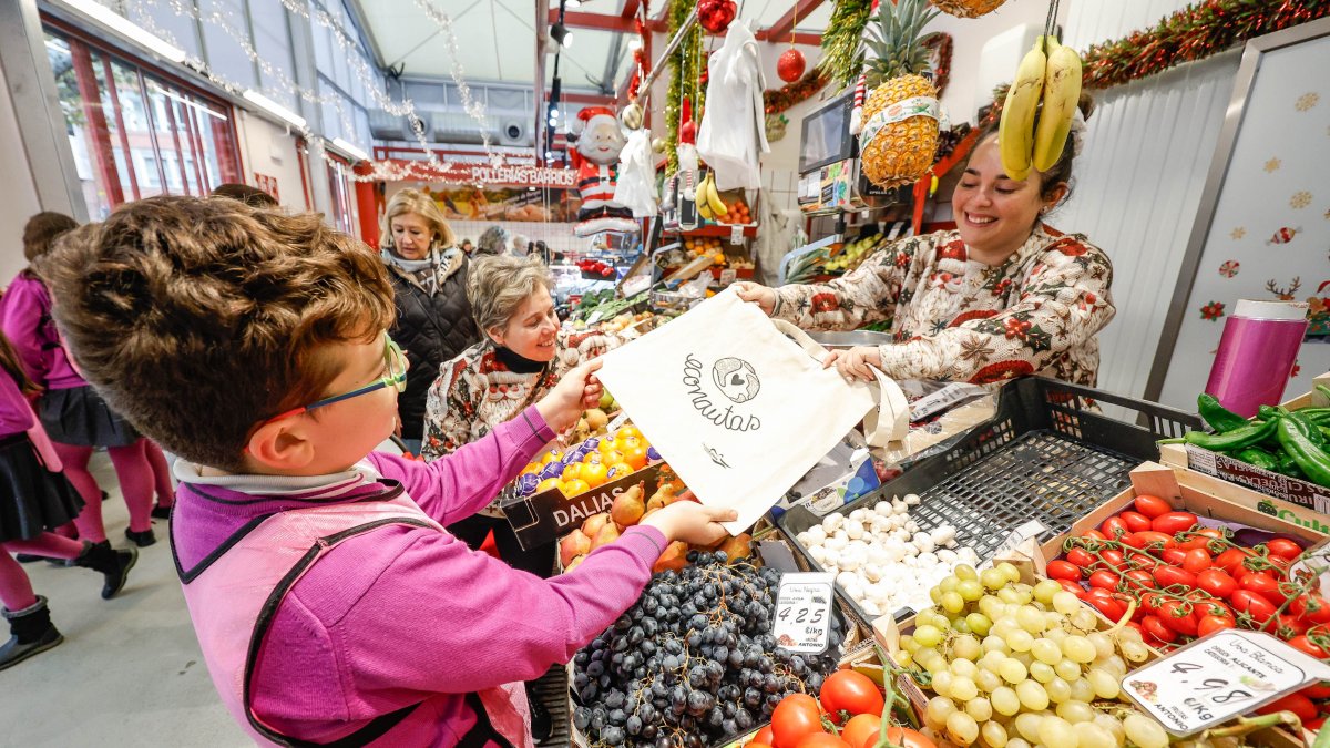 Un alumno del colegio Virgen de la Rosa entrega una de las bolsas de tela a una comerciante del mercado Norte provisional.