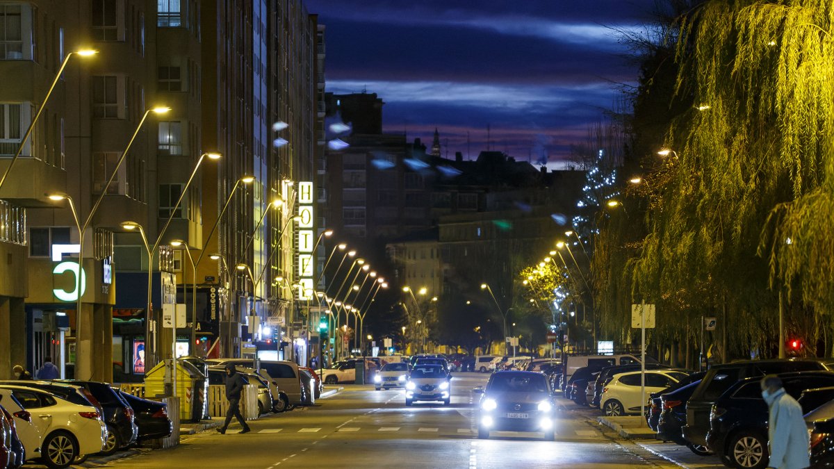 Un peatón cruza la avenida Reyes Católicos de noche, ya con el alumbrado público encendido.