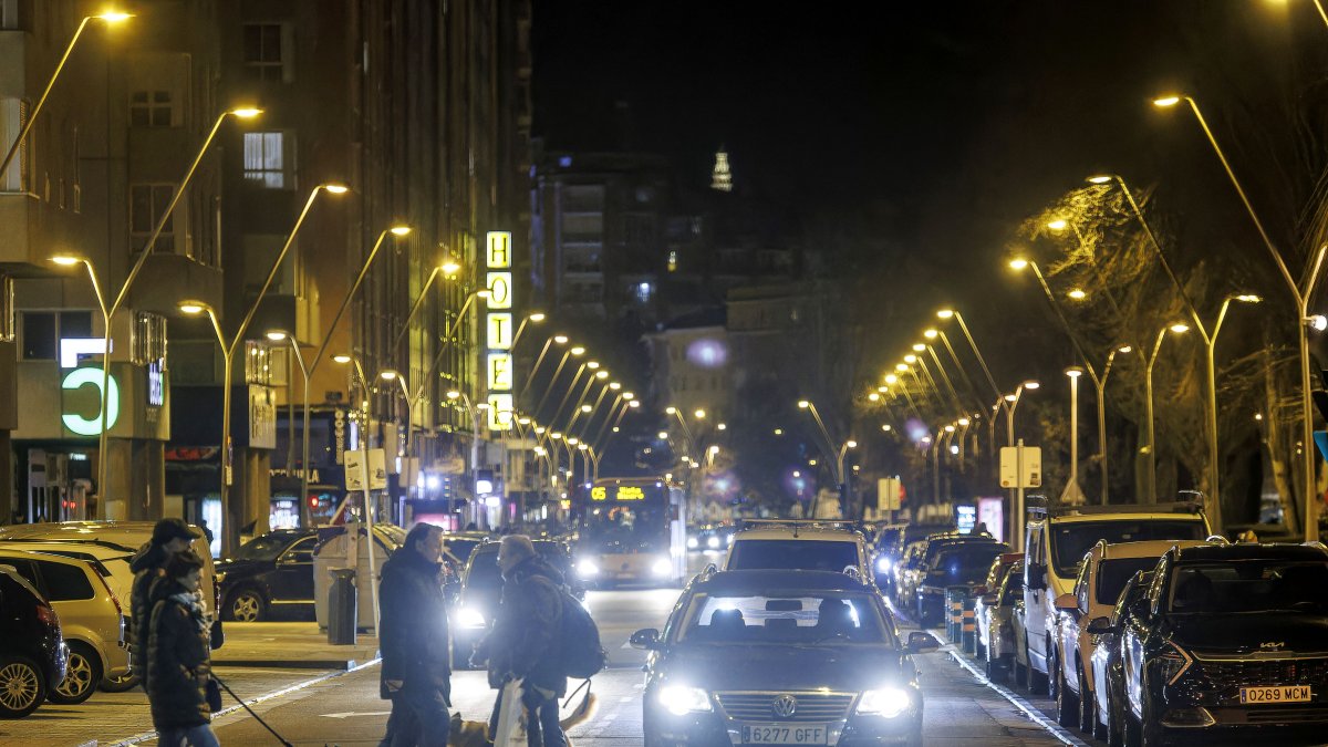 Peatones cruzando por la avenida Reyes Católicos, de Burgos, con el alumbrado público encendido.
