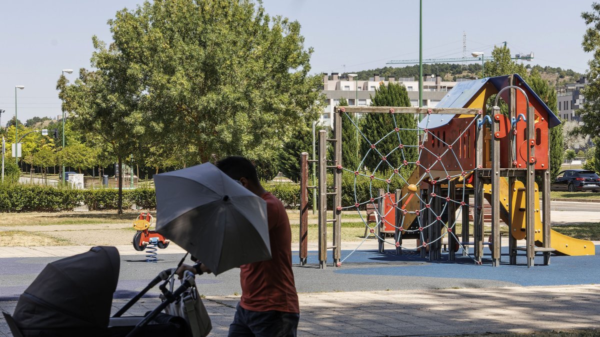 Un padre pasea con su bebé junto a un parque infantil en el paseo del Río Vena.