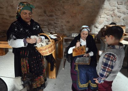 Un niño observa como dos mujeres cardan la lana.