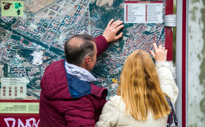 Dos turistas consultan uno de los mapas de la ciudad de Burgos instalado en un Mupi.