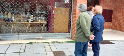 Dos personas observan la puerta rota con una alcantarilla para entrar a robar en un comercio de la calle San Pedro de Cardeña.